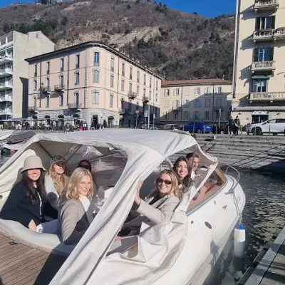 Group of people on a boat near a dock with buildings and hills in the background.