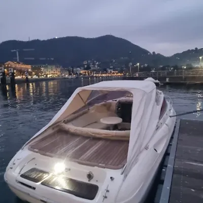 White boat docked at a pier with mountains and buildings in the background during dusk.