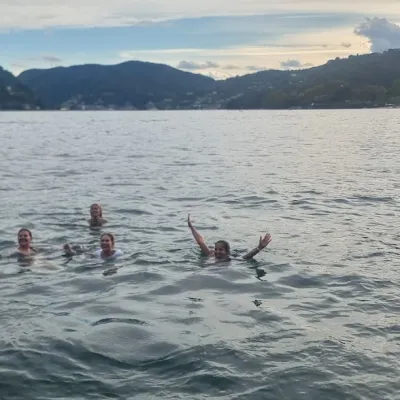 Four people swimming in a lake with hills and buildings in the background.