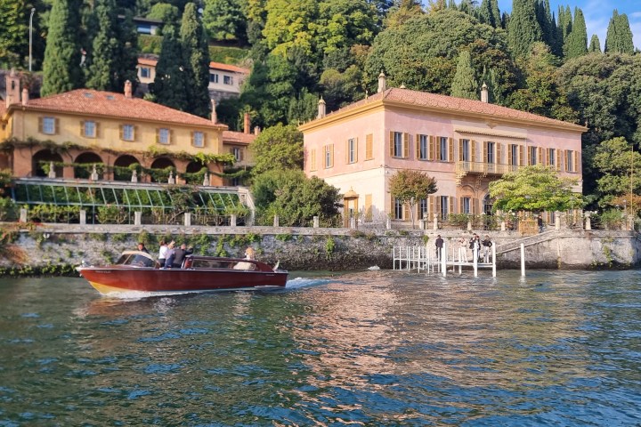 A boat on a lake in front of villas and lush greenery on a sunny day.
