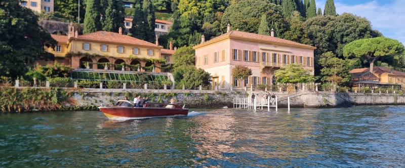 A boat on a lake in front of villas and lush greenery on a sunny day.