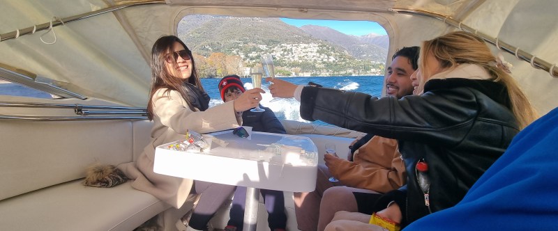 Group of people on a boat toasting with glasses in a scenic lake setting.