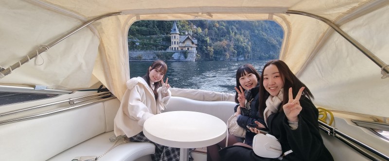 Three people smiling and posing with peace signs on a boat with a scenic river view.