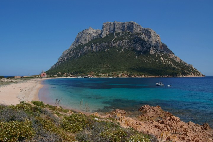 Coastal landscape with a mountain, blue sea, sandy beach, and small boat.
