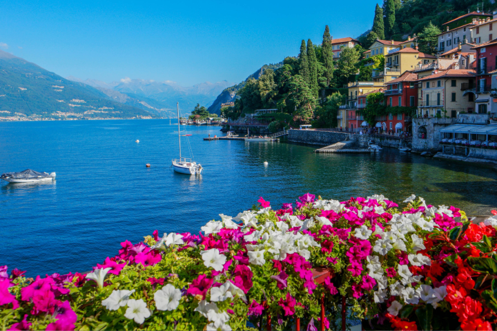 Colorful flowers in foreground, lake with boats, and hillside town in background.