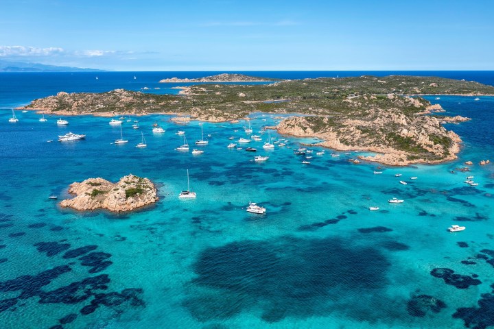 Turquoise sea with rocky islands and anchored sailboats under a clear blue sky.