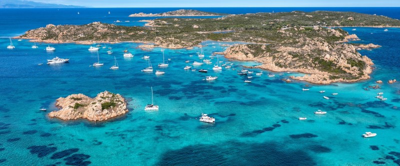 Turquoise sea with rocky islands and anchored sailboats under a clear blue sky.