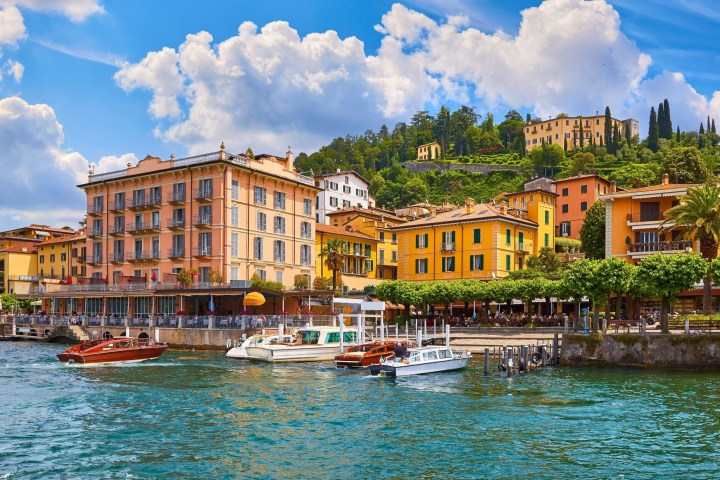 Colorful buildings by a lakeside with boats and a hillside in the background.