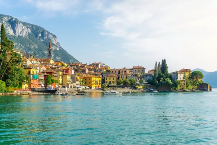 Colorful lakeside village with boats, surrounded by mountains and greenery.