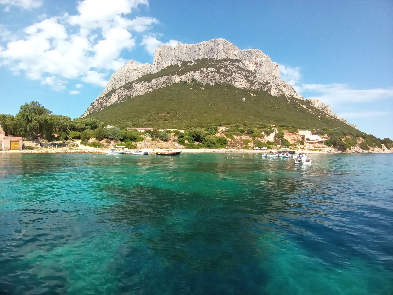 Scenic view of a mountain by the sea with clear turquoise water and some boats.