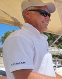 Smiling man in sunglasses and cap on a boat, wearing a white SALIMAR shirt.