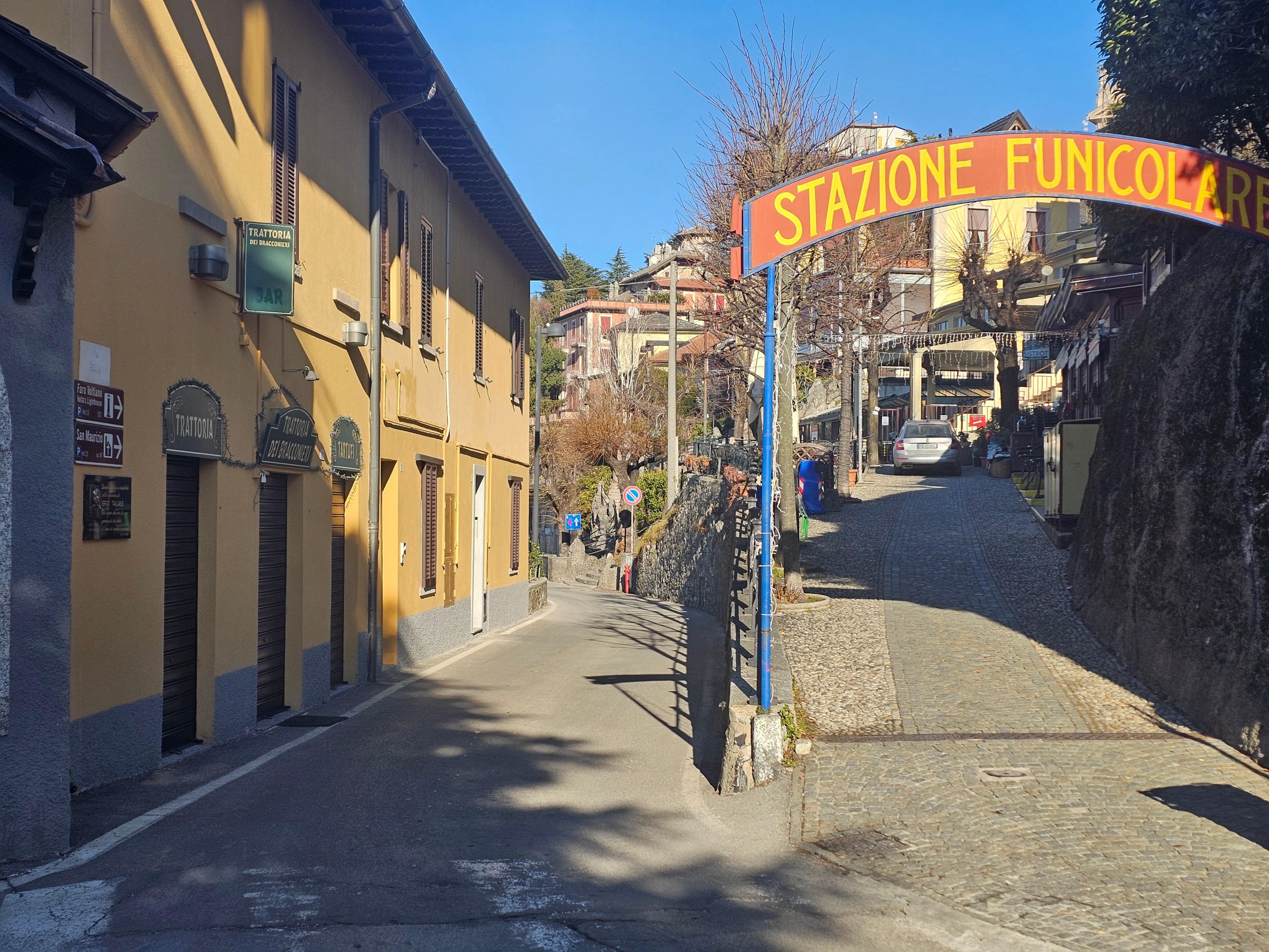 Sunny street with 'Stazione Funicolare' sign, yellow buildings, and cobblestone path.