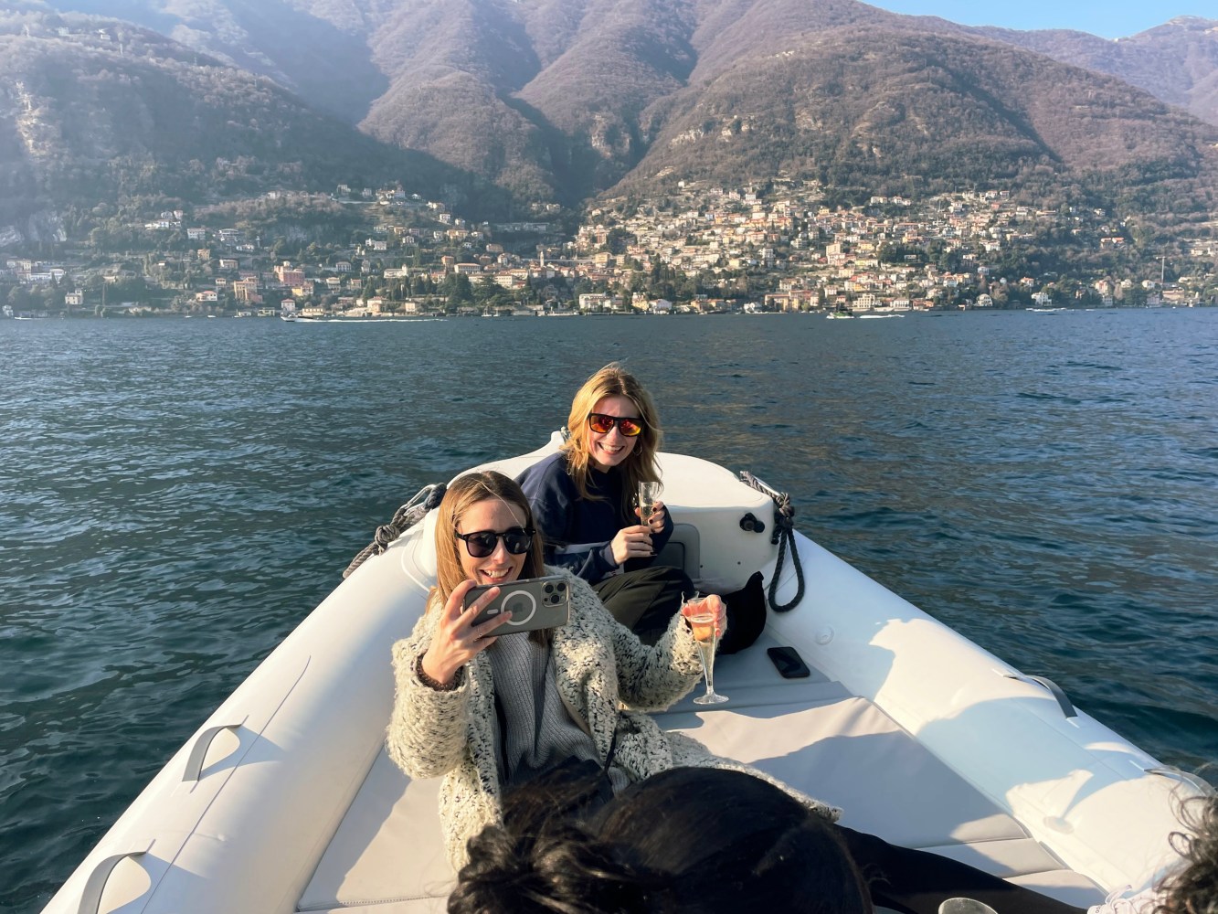 Two women on a boat taking selfies with mountains in the background.