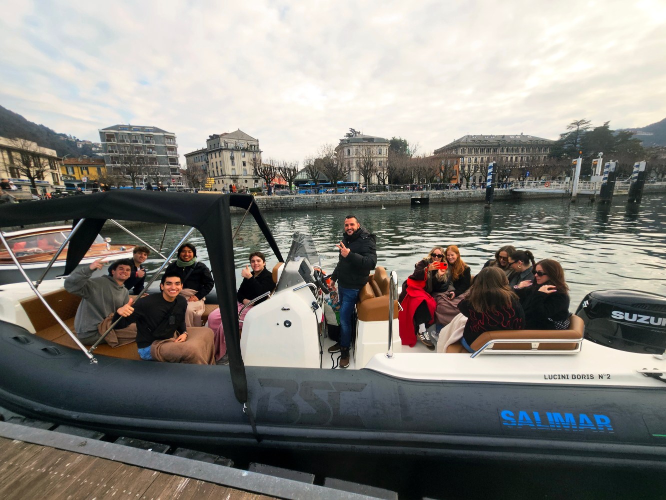 Group of people on a boat near a waterfront, with buildings in the background.